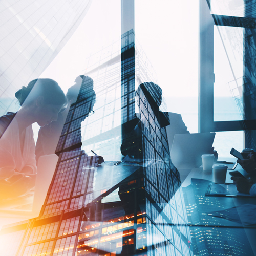 A group of professionals collaborates around a conference table, with laptops and documents in front of them. The image is overlaid with a city skyline, blending the indoor meeting with an urban landscape, suggesting themes of business and teamwork.