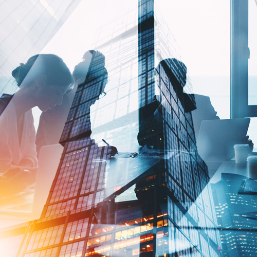A double exposure image depicts two business professionals engaged in a meeting, with a modern skyscraper reflected in the foreground. The scene conveys a sense of collaboration and urban professionalism, emphasizing the integration of work and architecture.