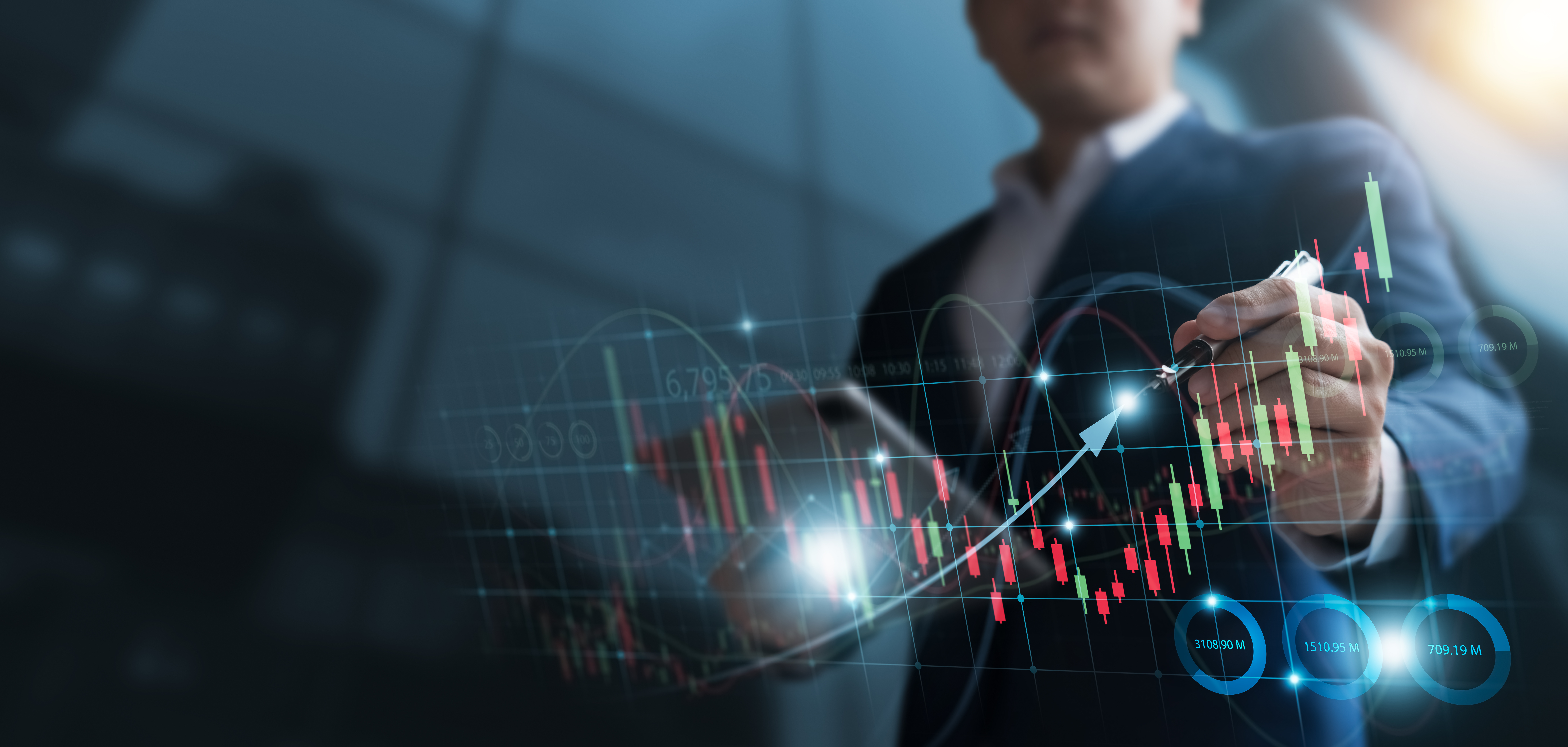 A business professional, dressed in a suit, uses a pen to highlight data on a digital screen displaying a financial chart. The chart features green and red candlestick patterns, indicating price movements, along with various numerical figures related to market analytics.