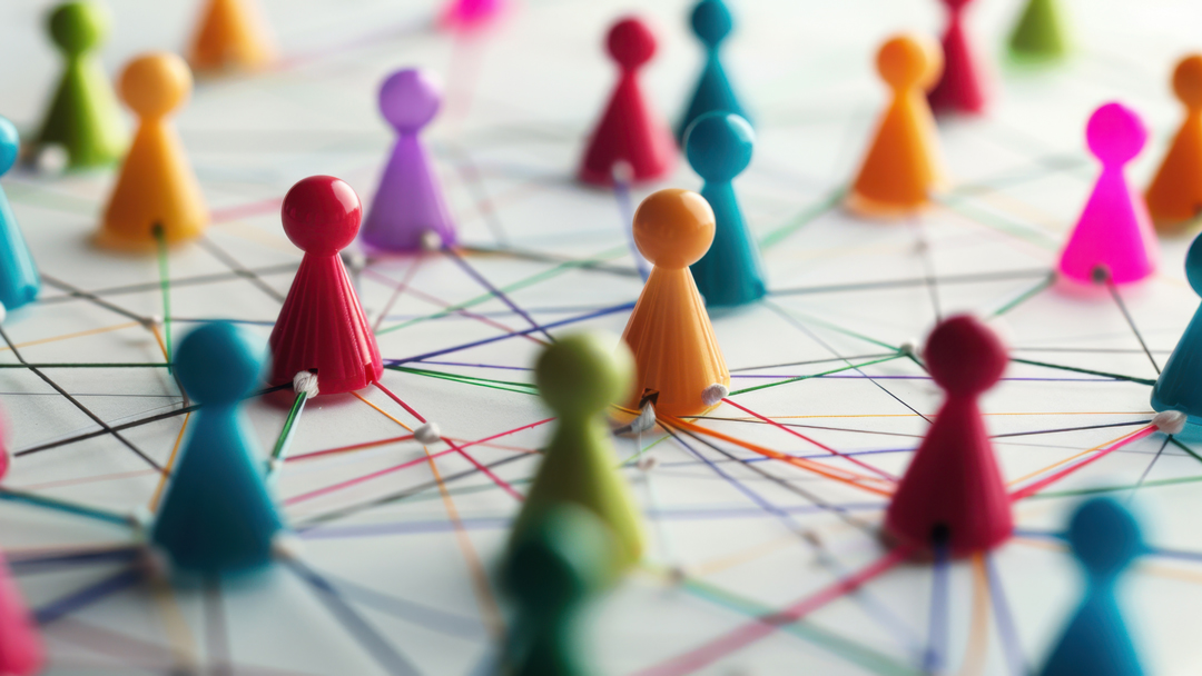 Colorful figurines are connected by various strings on a flat surface, representing a network or community. The arrangement illustrates interaction and connections among individuals, emphasizing collaboration and relationships within a group.