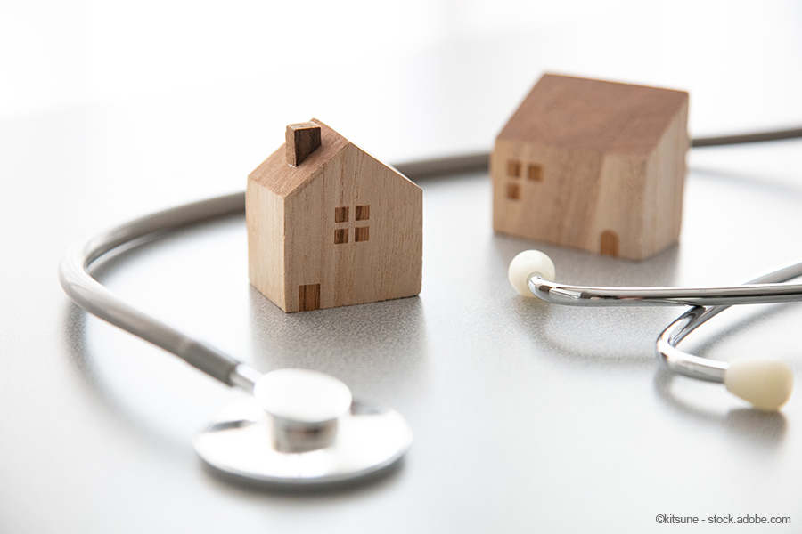 Two small wooden house models are placed on a light surface next to a stethoscope. The image symbolizes the connection between home and healthcare.