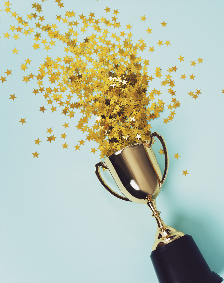 A golden trophy overflows with sparkling gold star confetti against a light blue background, symbolizing celebration and achievement.